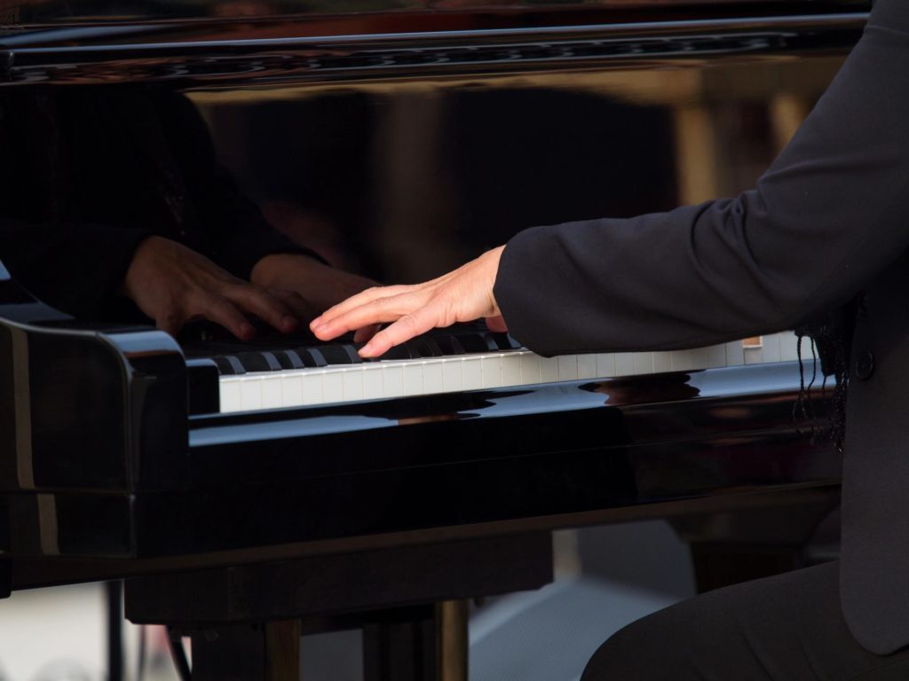 Close-up of hands playing a black grand piano.
